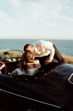 a man and woman are kissing in the back of a convertible car by the ocean