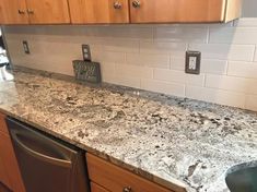 a granite counter top in a kitchen with wooden cabinets and stainless steel dishwasher