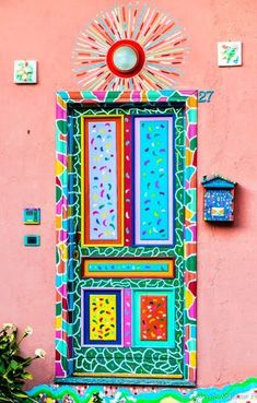 a colorful door is painted on the side of a pink building with flowers in front