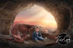 a little boy sitting on the ground next to a dragon in a cave at sunset