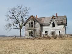 black and white photograph of an old house in the middle of a field with two trees