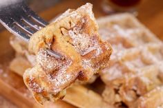 a fork with some food on it and powdered sugar in the middle, over waffles