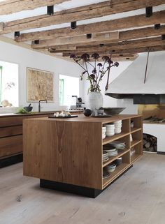 an open kitchen with wooden cabinets and white dishes on the counter top, in front of a fireplace