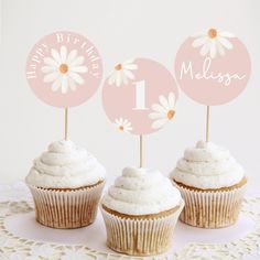 three cupcakes with white frosting and daisies are on a doily