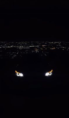 the headlights of a car are glowing in the dark at night with city lights behind them