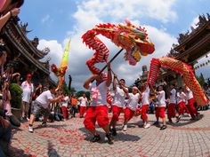 a group of people in red and white outfits are dancing with dragon shaped umbrellas