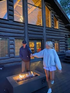 a man and woman standing in front of a fire pit on a deck next to a log cabin