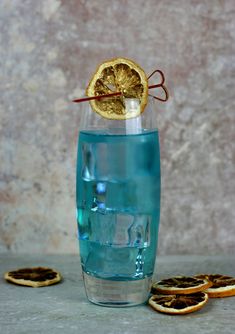 a glass filled with blue liquid next to sliced oranges