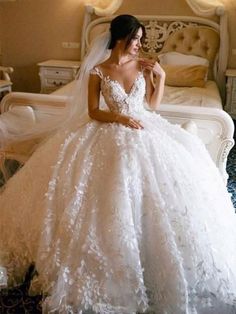 a woman in a white wedding dress sitting on a bed with her hand on her shoulder