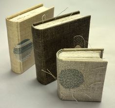 three books with thread on them sitting next to each other in front of a white background