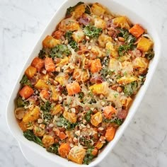 a casserole dish filled with vegetables and nuts on a marble countertop, ready to be eaten