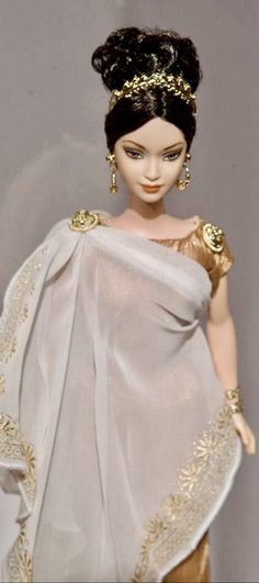 a doll wearing a white dress with gold accents on it's head and shoulders