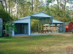 a blue shed with picnic tables and benches in the back yard next to some trees