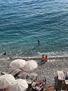 people are sitting on the beach with umbrellas and chairs near the water's edge