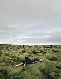 a woman laying on the ground covered in green mossy grass with her eyes closed