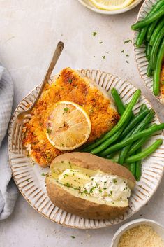 two plates with baked potatoes, green beans and lemon wedges on them next to some bread