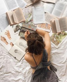 a woman laying on top of a bed with lots of open book pages around her