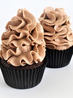 two cupcakes with chocolate frosting on top sitting side by side in front of each other