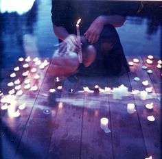 a person kneeling down on a wooden floor with candles in the water behind them,