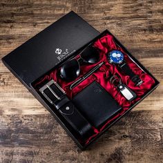 an open box containing a watch, sunglasses and wallet on a wooden table with a red cloth