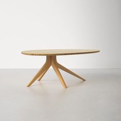 a round wooden table sitting on top of a white floor next to an empty wall