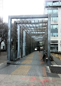 people are sitting on benches under an open metal structure in front of a large building