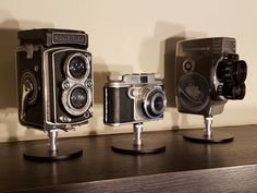 three old fashioned cameras sitting on top of a wooden table