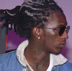 a man with dreadlocks wearing sunglasses and a denim jacket looks off to the side