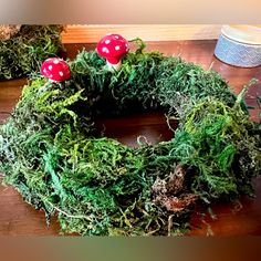 a moss wreath with two red mushrooms on the top and one green in the middle