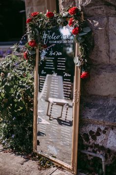 a sign with flowers on it sitting next to a stone wall in front of a building