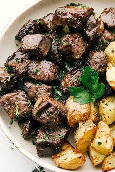 a white plate topped with meat and potatoes covered in parsley on top of a table