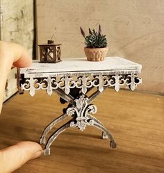 a miniature table with two potted plants on it and a hand holding the base