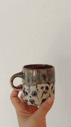 a hand holding a coffee cup with flowers on it in front of a white wall