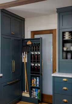 a kitchen with blue cabinets and gold pulls on the doors, an open pantry is in the center