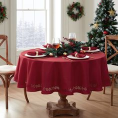 a christmas table setting with red cloths and place settings on it, surrounded by holiday wreaths