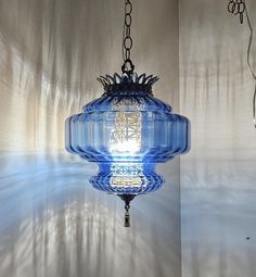 a blue glass light fixture hanging from a ceiling in a room with white walls and shadows on the wall