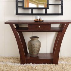 a vase sitting on top of a wooden table next to a mirror and wall hanging