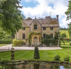 a large house sitting next to a pond in the middle of a lush green field