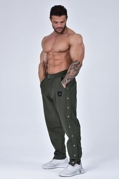 a shirtless man in green sweatpants and white sneakers posing with his hands on his hips