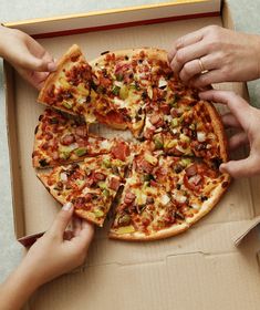 three people grabbing slices of pizza from a box