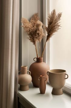 three vases are sitting on a window sill with some dried plants in them