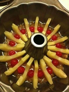 pineapples and cherries are arranged in the center of a metal bowl on top of a stove