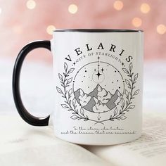 a black and white coffee mug sitting on top of an open book with the words velarriss