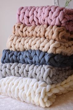 a pile of knitted blankets sitting on top of a white bed cover covered in blue, pink, and beige colors