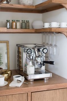 an espresso machine sitting on top of a wooden counter next to cups and saucers