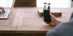 a person sitting at a table with a cell phone in front of their laptop computer