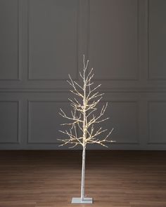 a white christmas tree with lights on it in front of a gray wall and wooden floor