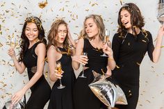 four women in black dresses holding champagne flutes and confetti buckets while standing next to each other