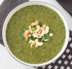 a bowl of green soup with cashews and spinach leaves on top, next to a napkin