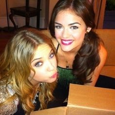 two beautiful young women sitting next to each other in front of an open pizza box